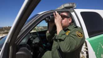 A U.S. Border Patrol agent looks through binoculars while patrolling.