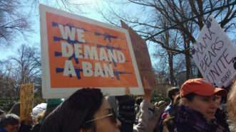 March for Our Lives protesters hold up a sign that says "WE DEMAND A BAN"
