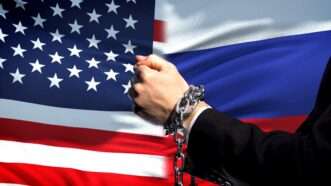 A side-by-side of the U.S. and Russian flags, with a person's handcuffed hands in the foreground