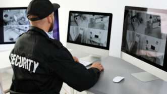 A security guard sits, monitoring home surveillance footage.