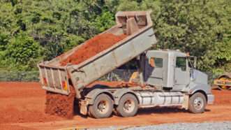 A tip truck dumping red soil at a construction site.