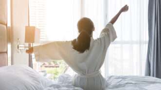 A woman wakes up in a hotel room and stretches.