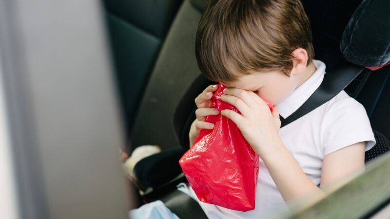 Child in the backseat with his face in a barf bag.