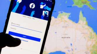 A smartphone on the Facebook login screen, against a world map of Australia in the background.