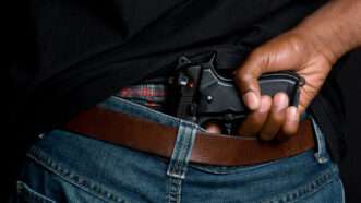 A man holds a gun in his rear wasteband.