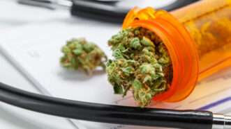 Close-up of marijuana in a prescription pill bottle, a stethoscope, and a prescription pad.