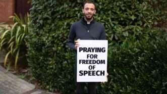 A man holding a sign reading "Praying for Free Speech"
