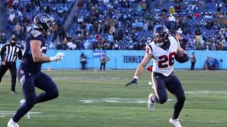 A Houston Texans player runs with the football, trying to evade a Tennessee Titans player.