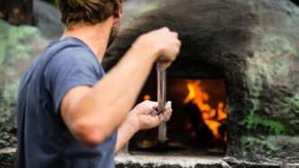 A cook shovels a pizza into a wood-fired stone pizza oven.