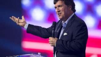 Tucker Carlson gesticulates while speaking on stage at Turning Point USA's December 2022 AmericaFest.