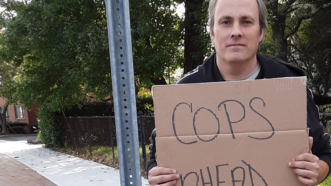 Michael Friend standing on the sidewalk holding a sign that reads 'cops ahead'