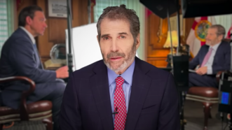John Stossel is seen in front of a still from his interview with Gov. Ron DeSantis