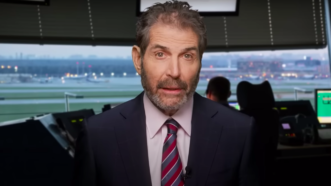 John Stossel is seen in front of an air traffic control system