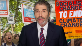 John Stossel stands in front of protest signs for socialist solutions to climate change