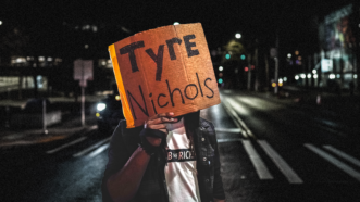 A person holds a Tyre Nichols sign at a protest against police brutality